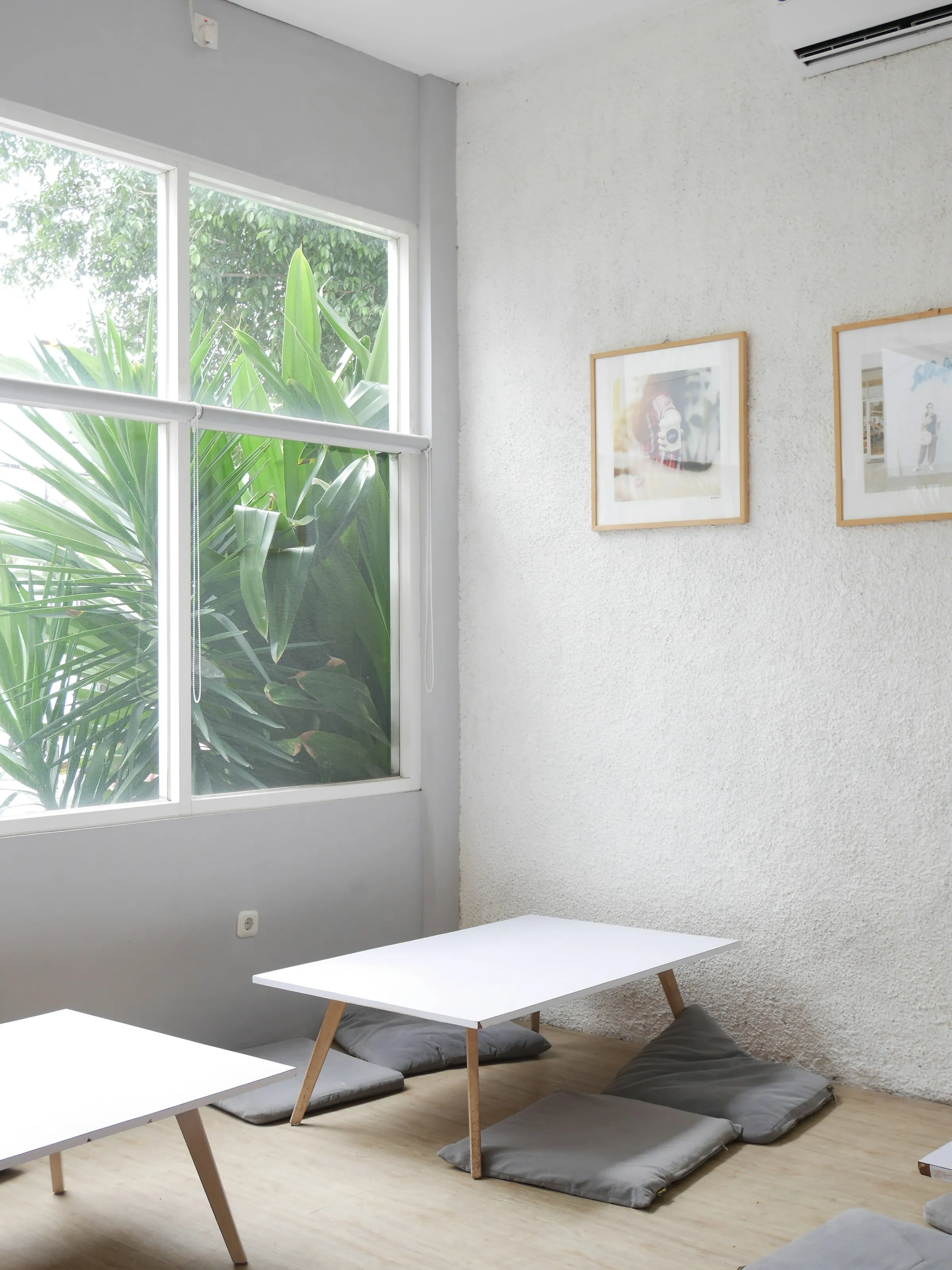 Bright white room with two low tables, gray floor cushions and a window looking onto green plants