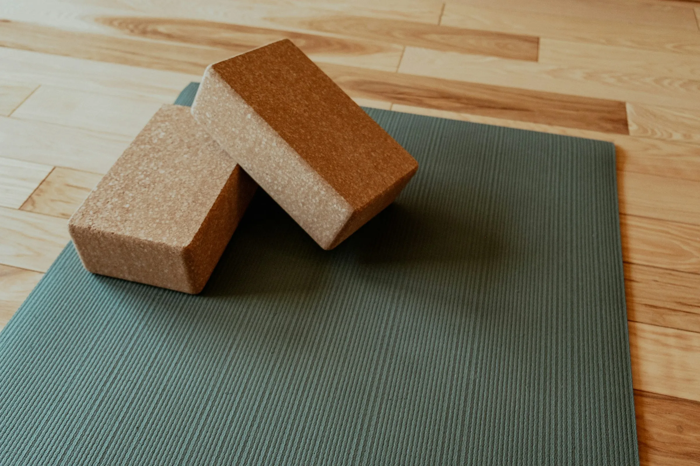 Two cork yoga blocks resting on a sage-green yoga mat on a light wooden floor