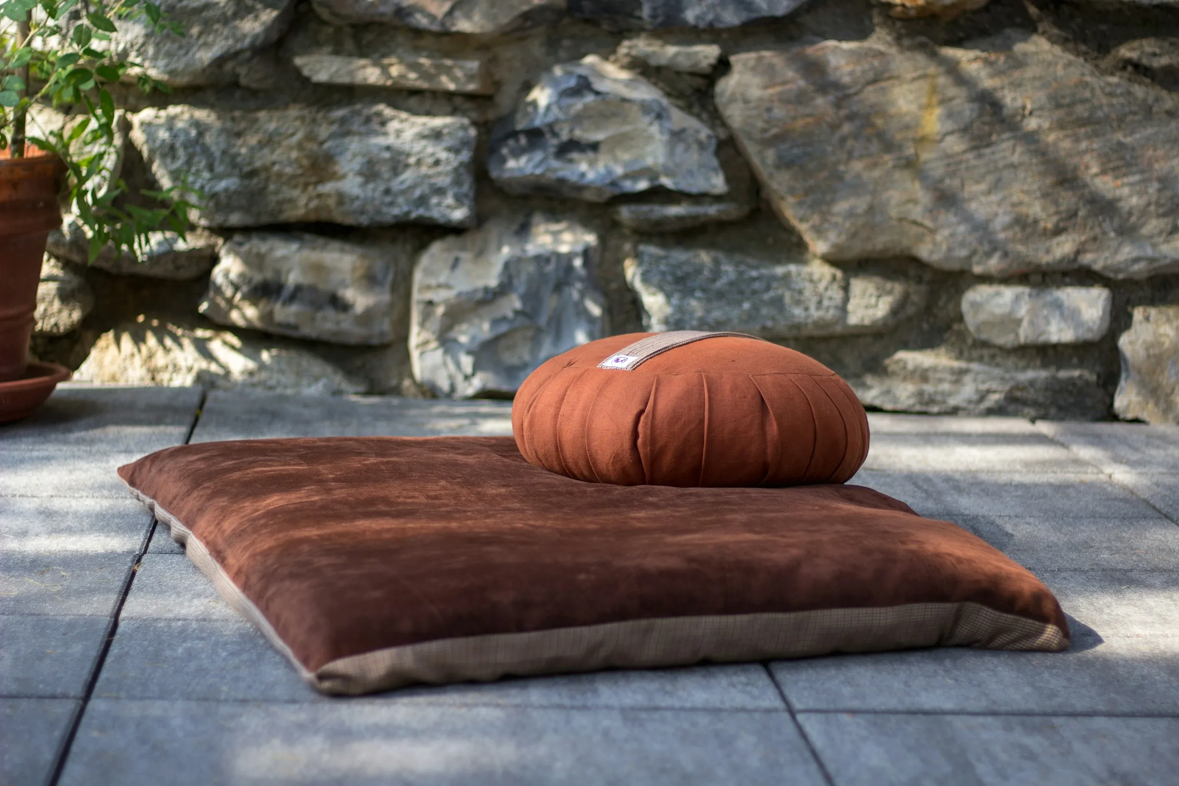 Round rust-colored zafu cushion on a brown square floor cushion on a stone terrace